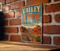 A vintage metal sign for Valley of Fire State Park in Nevada, featuring a desert landscape with mountains and a winding road.