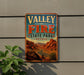 A vintage-style sign for Valley of Fire State Park, Nevada, featuring a desert landscape with mountains and a winding road.