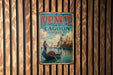 A vintage metal sign with the text "VENICE and its LAGOON ITALY" and an illustration of a gondola on the water, set against a wooden background.