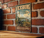 A vintage metal sign for Vickburg National Military Park in Mississippi, featuring a cannon and a steamboat, is displayed on a brick wall.