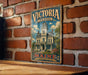 A vintage-style metal sign for "Victoria mansion" is displayed on a brick wall, featuring an illustration of a large, ornate mansion with a prominent tower.