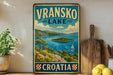 A vintage-style metal sign displaying the name "Vranksko Lake" and the word "Croatia" in bold letters, with a scenic illustration of a lake surrounded by mountains and islands.