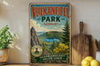 a vintage-style sign for Vulkaneefel Park, Germany, with a scenic mountain landscape and lake in the background.