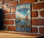 A vintage metal sign with a picture of a sailboat and a bird, mounted on a brick wall.