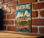 A vintage metal sign displaying the name "WARTBURG CASTLE" and the word "GERMANY" is hanging on a brick wall.
