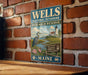 A vintage metal sign for the Wells National Estuarine Research Reserve in Maine, featuring a seagull and a lighthouse in a coastal landscape.