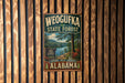 A vintage metal sign for Weoguffee State Forest in Alabama, featuring a scenic landscape with a lake and mountains.