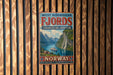 A vintage-style poster advertising West Norwegian Fjords, featuring a scenic image of a waterfall and mountains, is displayed on a wooden wall.