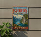 A vintage-style sign advertising West Norwegian Fjords, featuring a scenic image of a waterfall and mountains, with the text "NORWAY NATURE'S MASTERPIECE".
