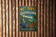 A vintage-style metal sign advertising the Wet Tropics of Queensland, Australia, featuring a colorful illustration of a tropical landscape with a bird and flowers.