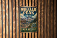 A vintage metal sign for Wheeler Peak Trail in New Mexico, featuring a mountain landscape and trail information.