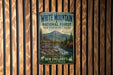A vintage metal sign for White Mountain National Forest in New Hampshire, Maine, featuring a scenic mountain landscape and inviting visitors to explore the area.