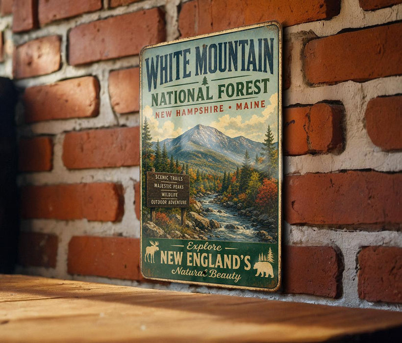 A vintage-style metal sign advertising White Mountain National Forest in New Hampshire and Maine, featuring a scenic mountain landscape and inviting visitors to explore the area.