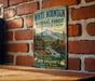 A vintage-style metal sign advertising White Mountain National Forest in New Hampshire and Maine, featuring a scenic mountain landscape and inviting visitors to explore the area.