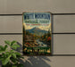 A vintage-style metal sign advertising the White Mountain National Forest in New Hampshire, Maine, with a scenic mountain landscape and trail information.