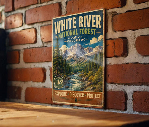 A vintage-style metal sign for the White River National Forest in Colorado, featuring a scenic mountain landscape with a river and pine trees.