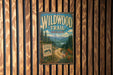 A vintage-style metal sign for the Wildwood Trail in Oregon, featuring a scenic mountain landscape and a road leading through the forest.