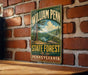 A vintage-style metal sign for William Penn State Forest in Pennsylvania, featuring a scenic landscape with pine trees and a lake.