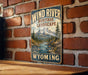 A vintage-style metal sign with the text "Wind River Heritage Landscape" and "Wild Scenic Rockies Wyoming" is displayed on a brick wall.
