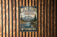 A vintage-style metal sign with the text "Wind River Heritage Landscape" and "Wild Scenic Timepieces Wyoming" is displayed on a wooden wall.