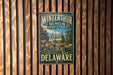 A vintage-style metal sign for the Winterthur Museum and Country Estate in Delaware, featuring a large illustration of a historic building surrounded by trees and flowers.