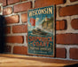 A vintage Wisconsin shipwreck coast sign is displayed on a brick wall, with a wooden table below it.