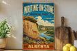A vintage-style sign for Writing on Stone Provincial Park in Alberta, Canada, featuring a scenic landscape with rock formations and a river.