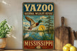 A vintage-style metal sign for the YAZOO NATIONAL WILDLIFE REFUGE in Mississippi, featuring a duck flying over a pond and surrounded by lush greenery.