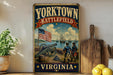 A vintage-style metal sign with the text "YORKTOWN BATTLEFIELD VIRGINIA" and an illustration of a cannon, two men in military uniforms, and a ship in the ocean.