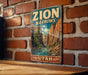 A vintage-style metal sign with the text "ZION NARROWS" and "UTAH" is displayed on a brick wall.