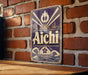 a vintage-style sign with the word "Aichi" prominently displayed, mounted on a brick wall.