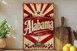 a vintage-style sign with the word "Alaska" prominently displayed, along with a sunburst design and a depiction of a state building. The sign is placed on a wooden surface, surrounded by various kitchen utensils and a potted plant.