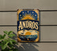 A vintage-style metal sign with the word "ANDROS" prominently displayed, featuring a lighthouse and a sunset in the background.