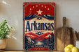 A vintage-style sign for Arkansas, featuring a red, white, and blue design with a star and mountains, is displayed on a shelf next to a wooden cutting board and some lemons.