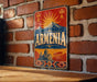 A vintage-style metal sign with the word "ARMENIA" prominently displayed, featuring a mountain, sun, and other traditional elements.