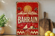 a vintage-style sign with the word "BAHRAIN" prominently displayed, along with a sailboat and a city skyline. The sign is placed on a wooden surface, surrounded by various kitchen utensils and a potted plant.