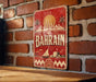 A vintage-style metal sign with the word "BAHRAIN" prominently displayed, featuring a cityscape and palm trees.