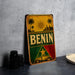 A vintage-style metal sign with the word "BENIN" prominently displayed, featuring a tropical landscape with palm trees and a sun.