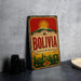 A vintage-style metal sign with the word "BOLIVIA" prominently displayed, featuring a sun and mountains in the background.