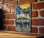 A vintage-style metal sign with the text "Bosnia and Herzegovina" displayed prominently against a brick wall background.
