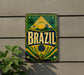 A vintage metal sign with the word "BRAZIL" prominently displayed, featuring a tropical landscape with palm trees and a sun.