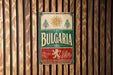 A vintage metal sign with the word "Bulgaria" displayed prominently, featuring a sun and floral design.