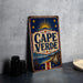 A vintage-style metal sign with the text "CAPE VERDE" displayed prominently, featuring a sun and stars design. The sign is placed on a gray surface, with a stack of black camera lenses and a white dish visible in the background.