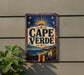 A vintage-style sign for Cape Verde beer is displayed on a wall, featuring a sun and stars design and a tropical landscape.