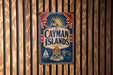 A vintage metal sign with the text "CAYMAN ISLANDS" and various symbols, including a British flag, a palm tree, and a ship, is displayed on a wooden wall.