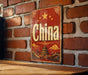 A vintage-style sign with the word "China" prominently displayed, featuring a traditional Chinese temple and a star in the background.