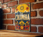 A vintage-style metal sign with the word "COLOMBIA" prominently displayed, featuring a sun, palm trees, and other tropical elements.