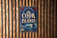 A vintage-style sign that reads "COOK ISLANDS" is displayed on a wooden wall.
