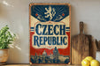 A vintage-style sign for the Czech Republic, featuring a lion and a castle, is displayed on a shelf next to a wooden cutting board and some lemons.