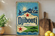 A vintage-style sign with a blue background and a white border, featuring illustrations of a sailboat, a lighthouse, and a palm tree, along with the text "Djibouti" prominently displayed.